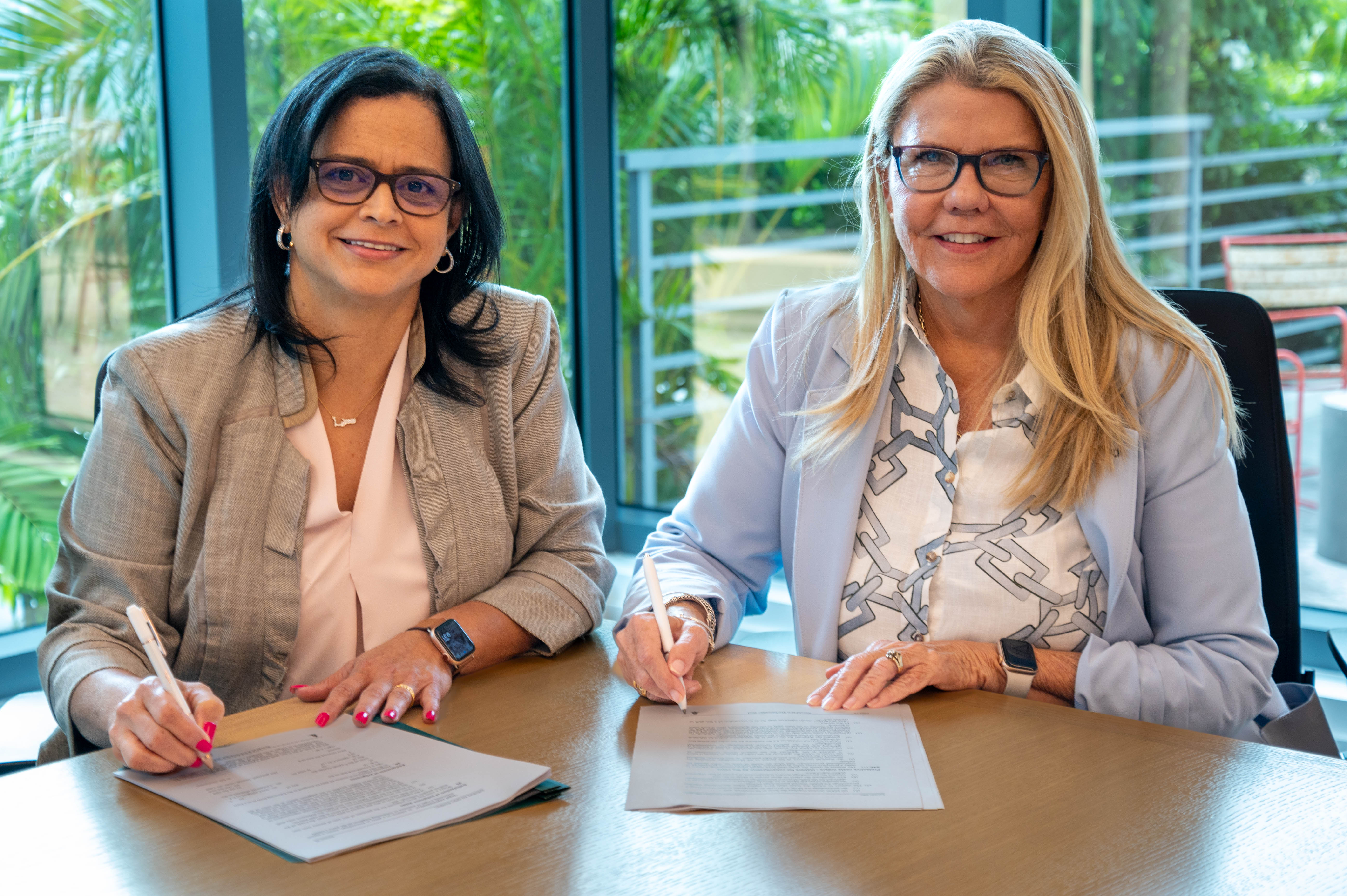 Photo of CIMA Managing Director Cindy Scotland and CIIPA CEO Sheree Ebanks sitting together at a table while signing documents. 